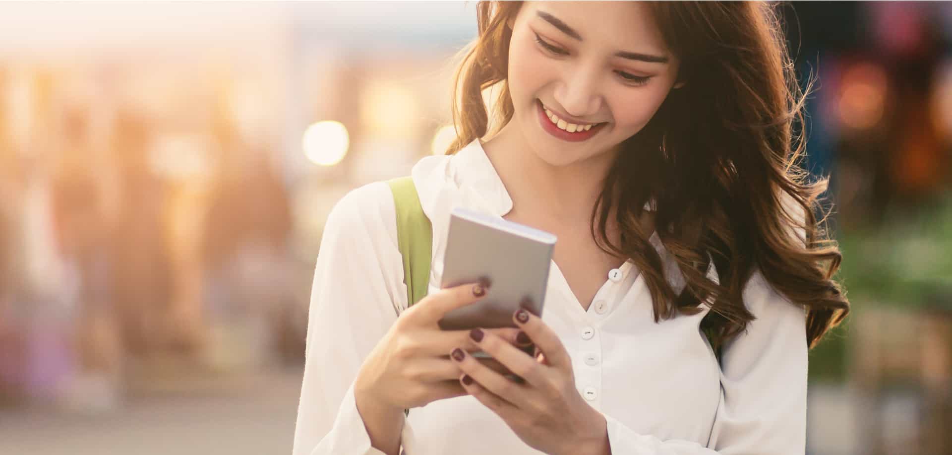 A woman smiling at her smartphone while using an SMS keyword service.